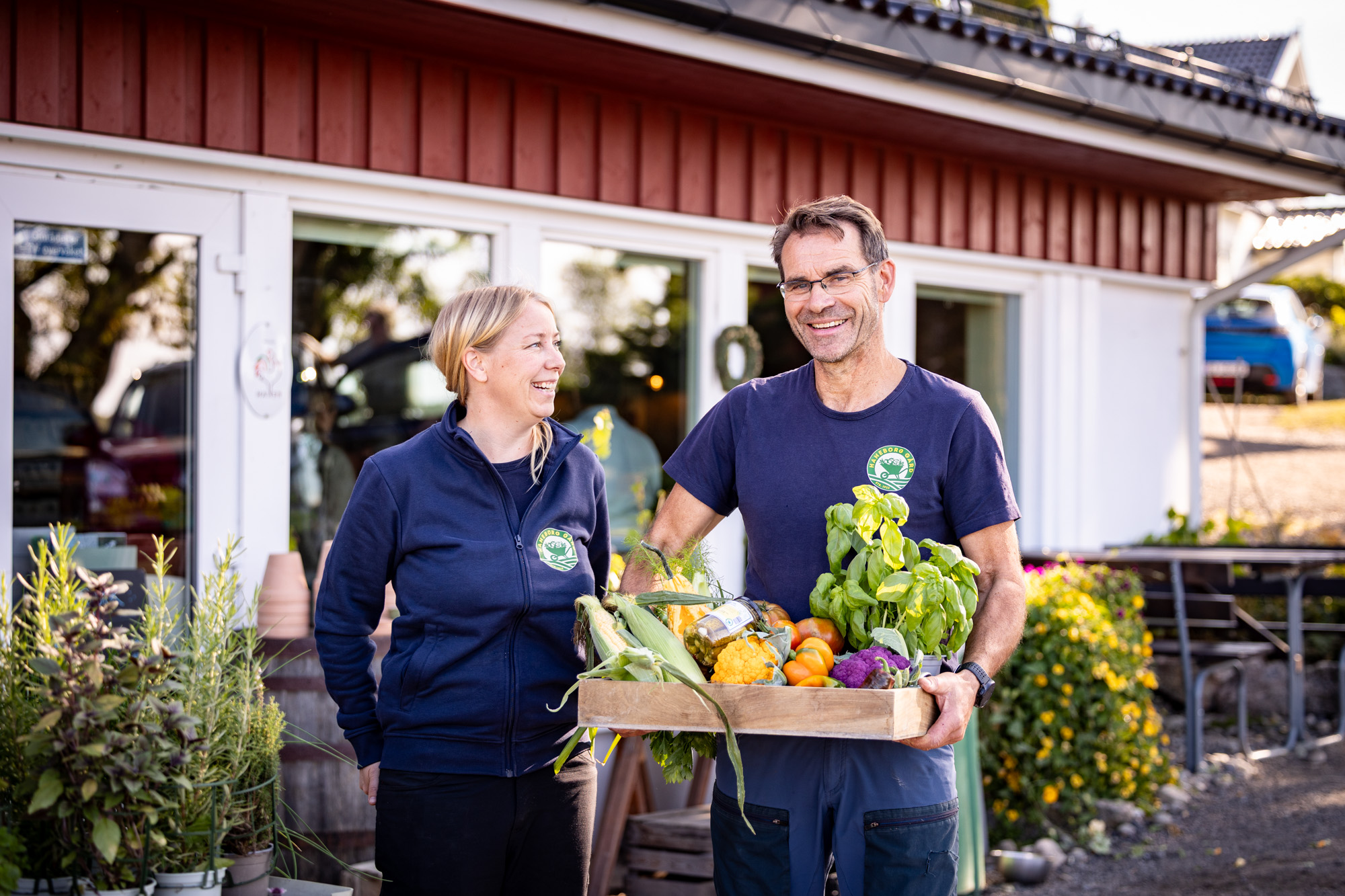 To produsenter står foran Haneborg gård med en kasse nyhøstede grønnsaker